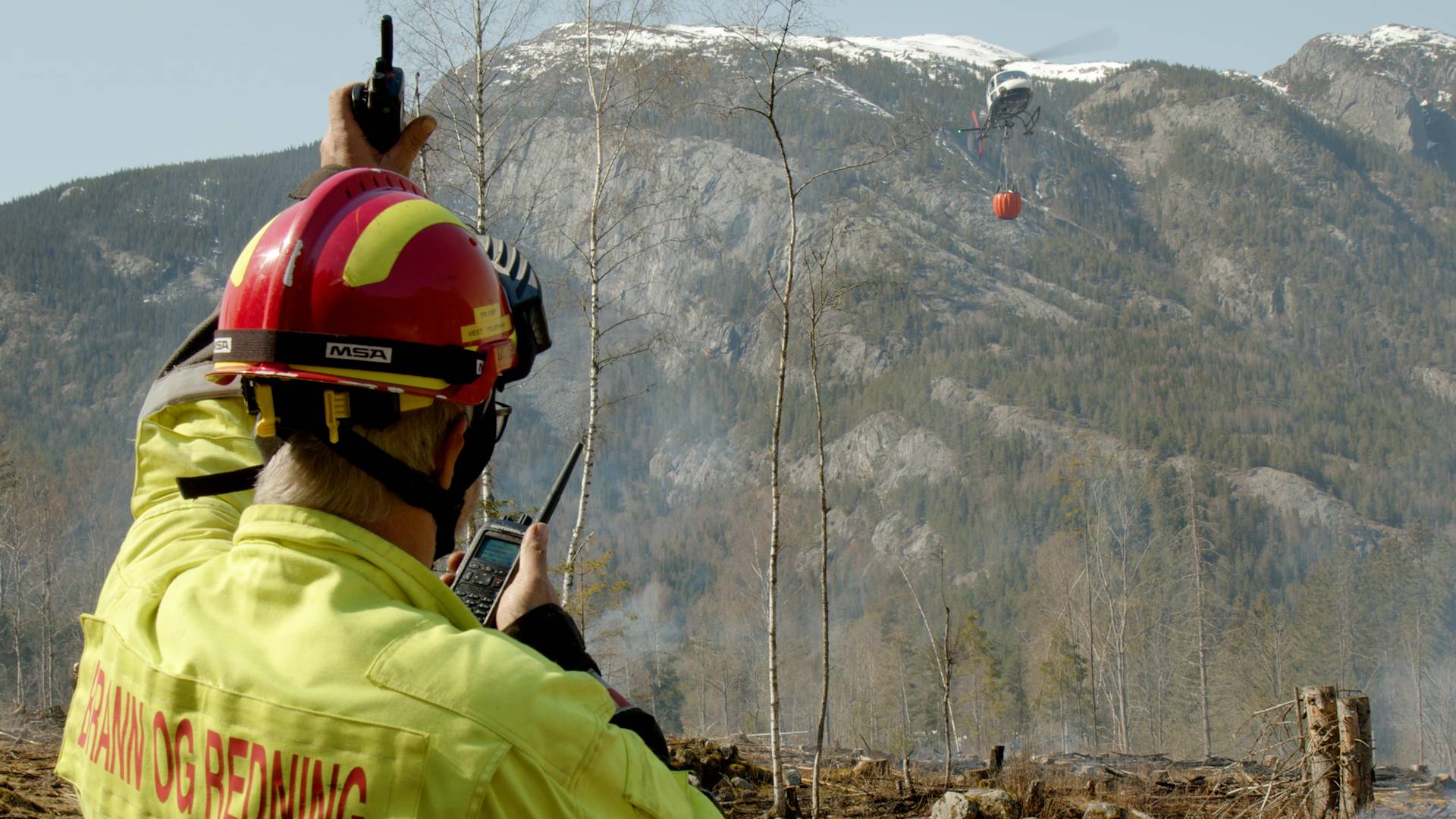 Illustrasjonsfoto av en redningsarbeider som snakker i en satelittelefon med en bil i bakgrunnen.