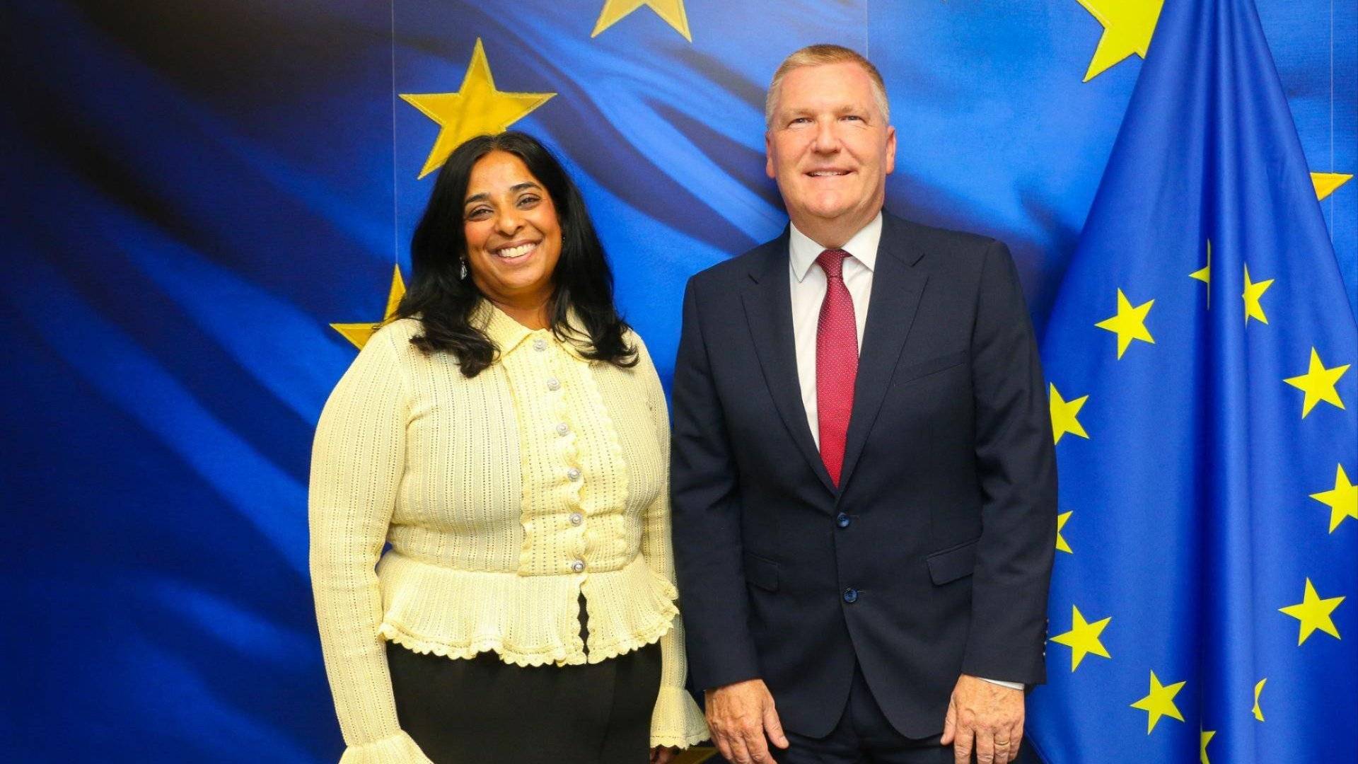 Bilde av Lubna Jaffery og Michael McGrath som står foran EU-flagget.