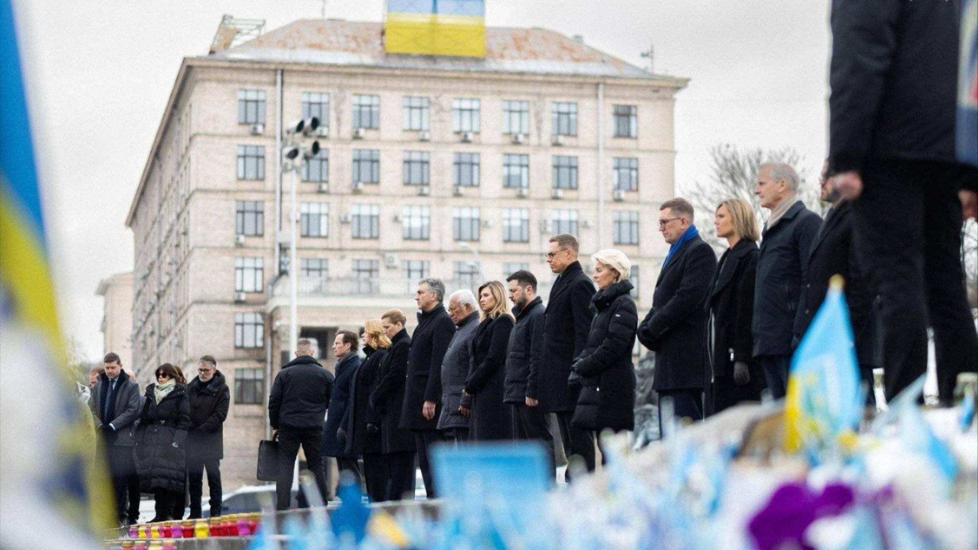 Bilde av to menn i dress som står foran en pressevegg og ser inn i kameraet mens de smiler